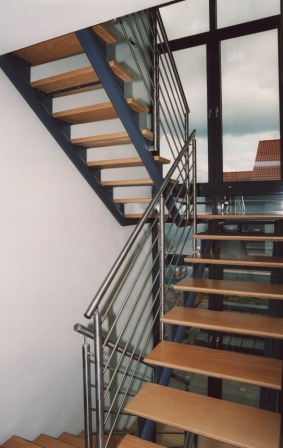 Innengeländer als Metallgeländer an einer Podesttreppe, diese Metalltreppe ist als Rundholmtreppe mit einem Zwischenpodest ausgeführt, das Treppengeländer ist in Edelstahl, die Trittstufen sind als Holzstufen ausgeführt