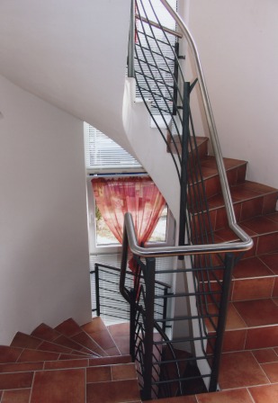 Stahlgeländer mit einem durchgehenden Handlauf in Edelstahl an einer gewendelten Betontreppe als Treppengeländer